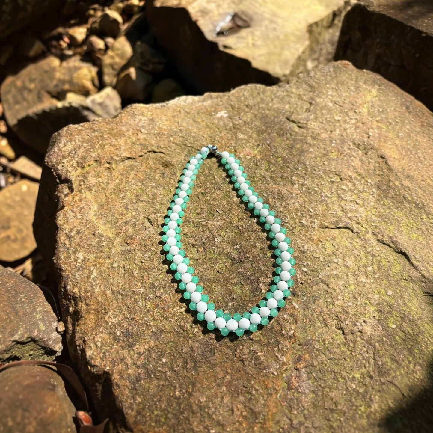 Hollywood Road Stories beaded choker necklace with alternating white and sage green beads on a textured stone background.