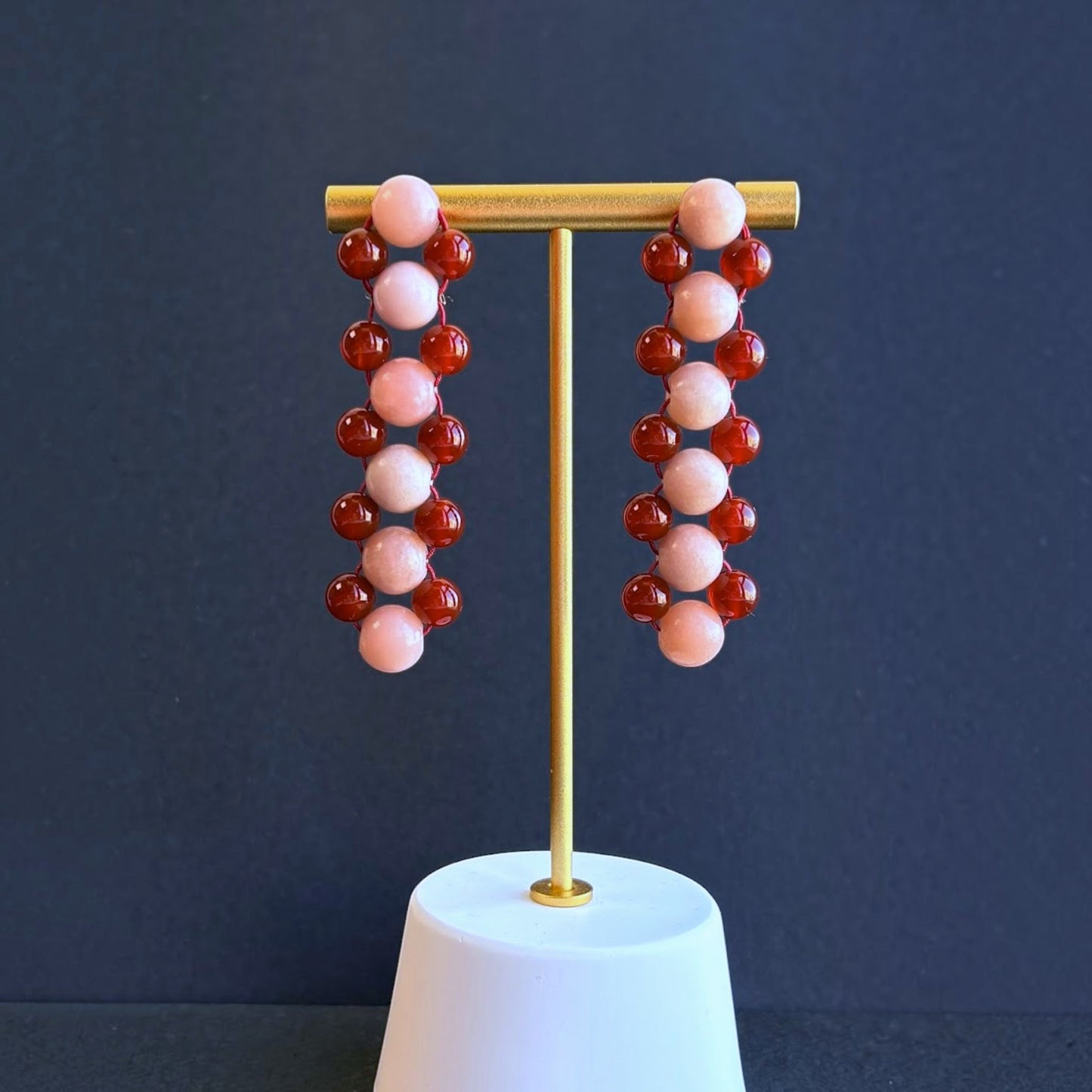 Hollywood Road Stories handcrafted drop earrings with alternating pink and deep red beads on a gold display stand.