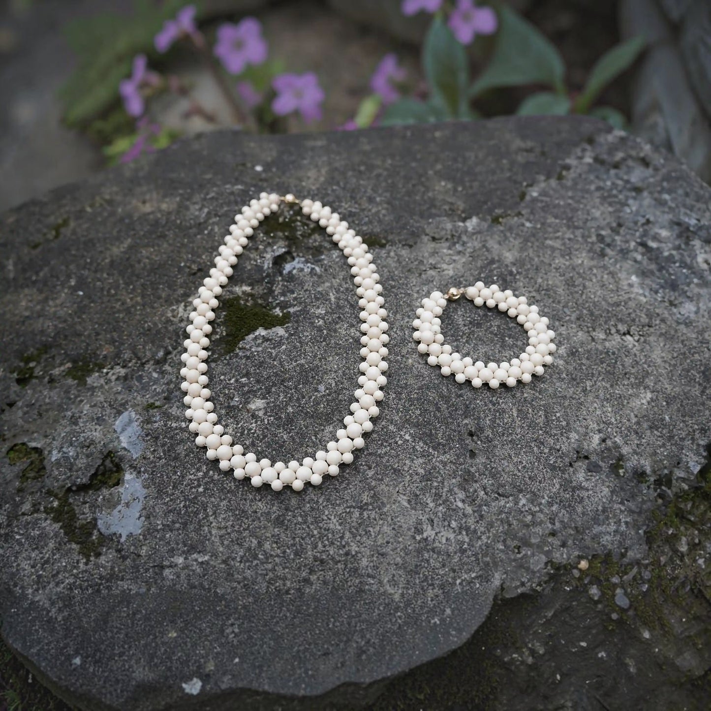 Hollywood Road Stories double strand cream beaded necklace and matching bracelet set on a textured stone surface
