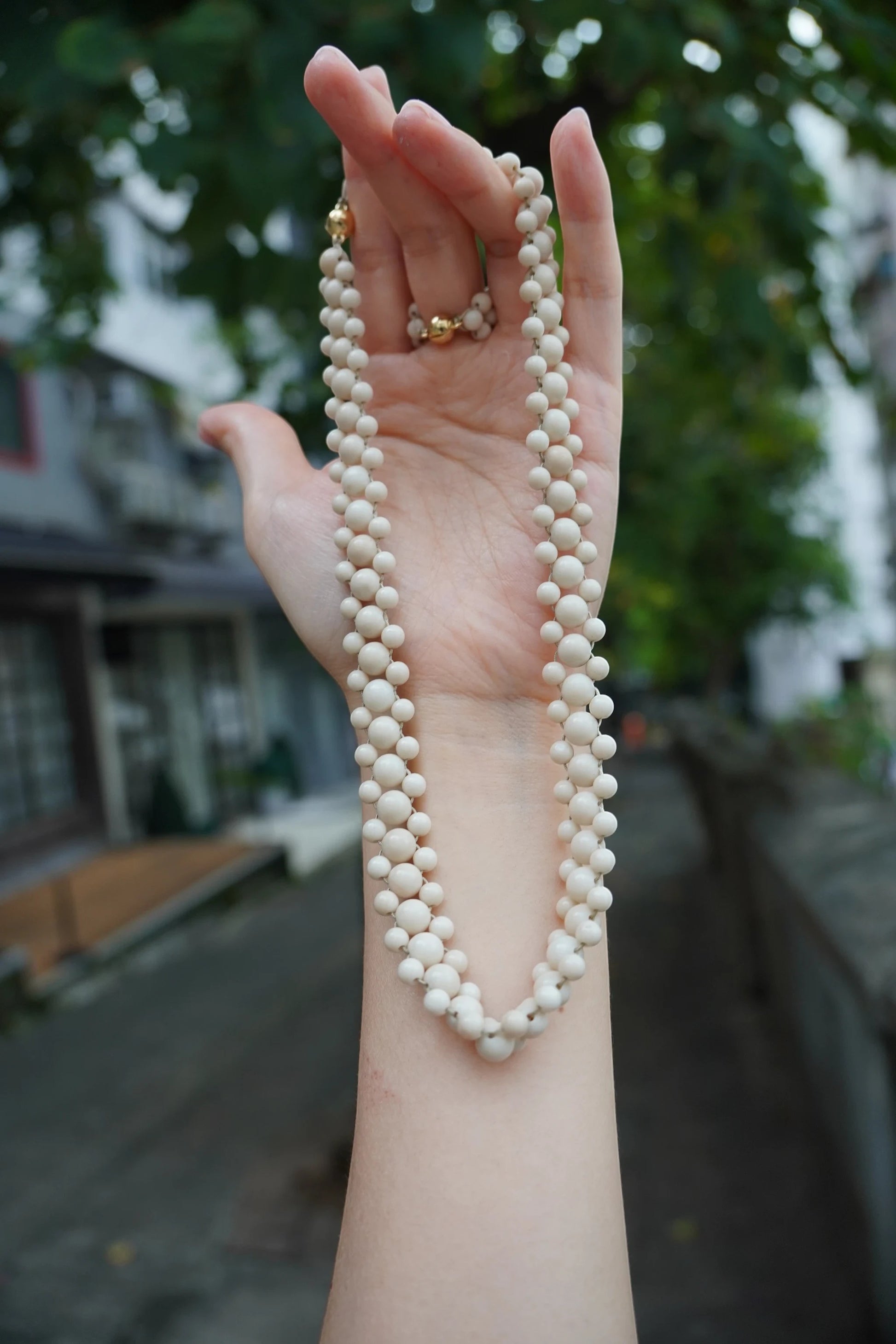 Hollywood Road Stories double strand cream beaded necklace with gold-tone clasp held in a hand