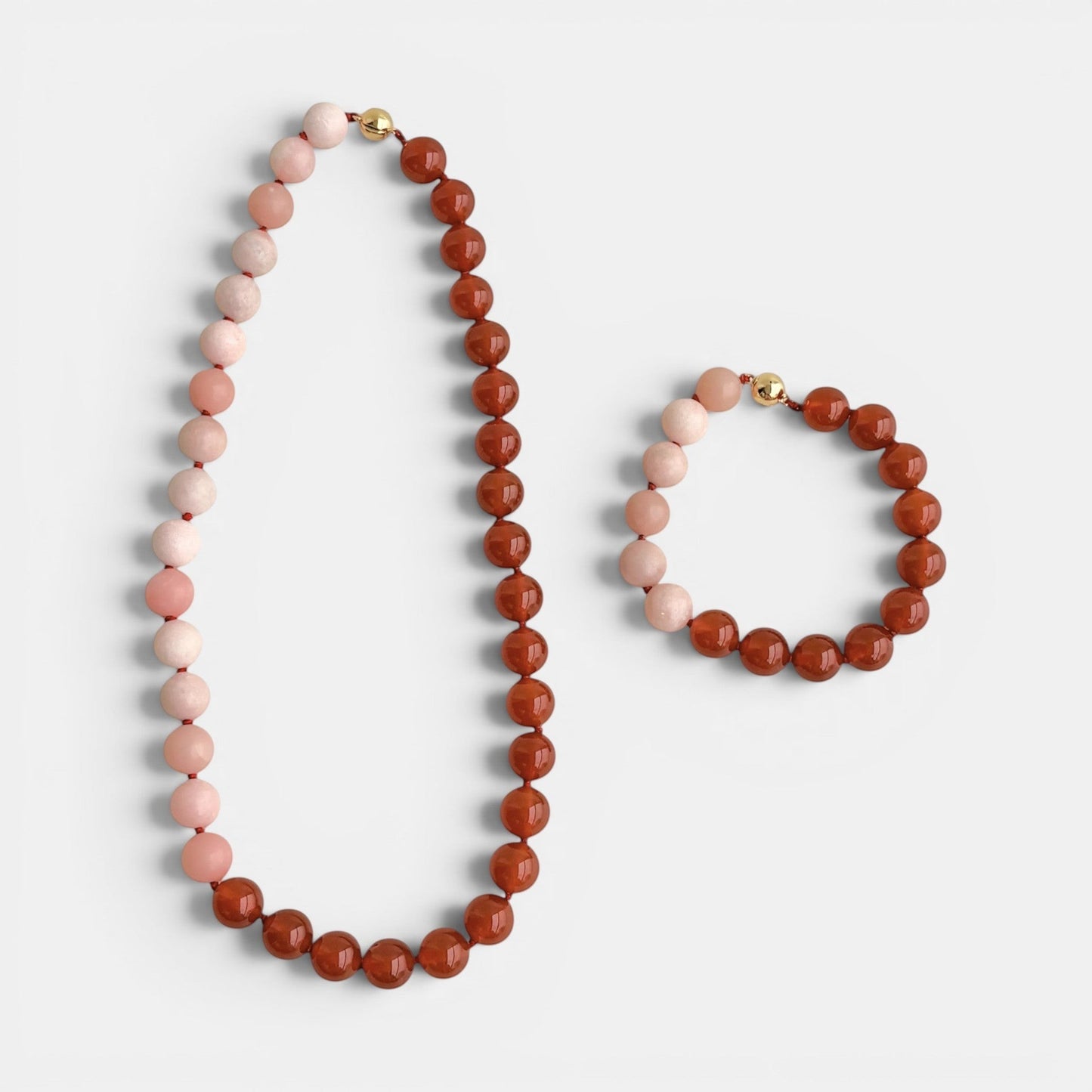 A matching jewelry set from Hollywoodroadtories Hong Kong, featuring a statement beaded necklace and a bracelet, both made of alternating light pink and red agate beads with gold magnetic clasp.