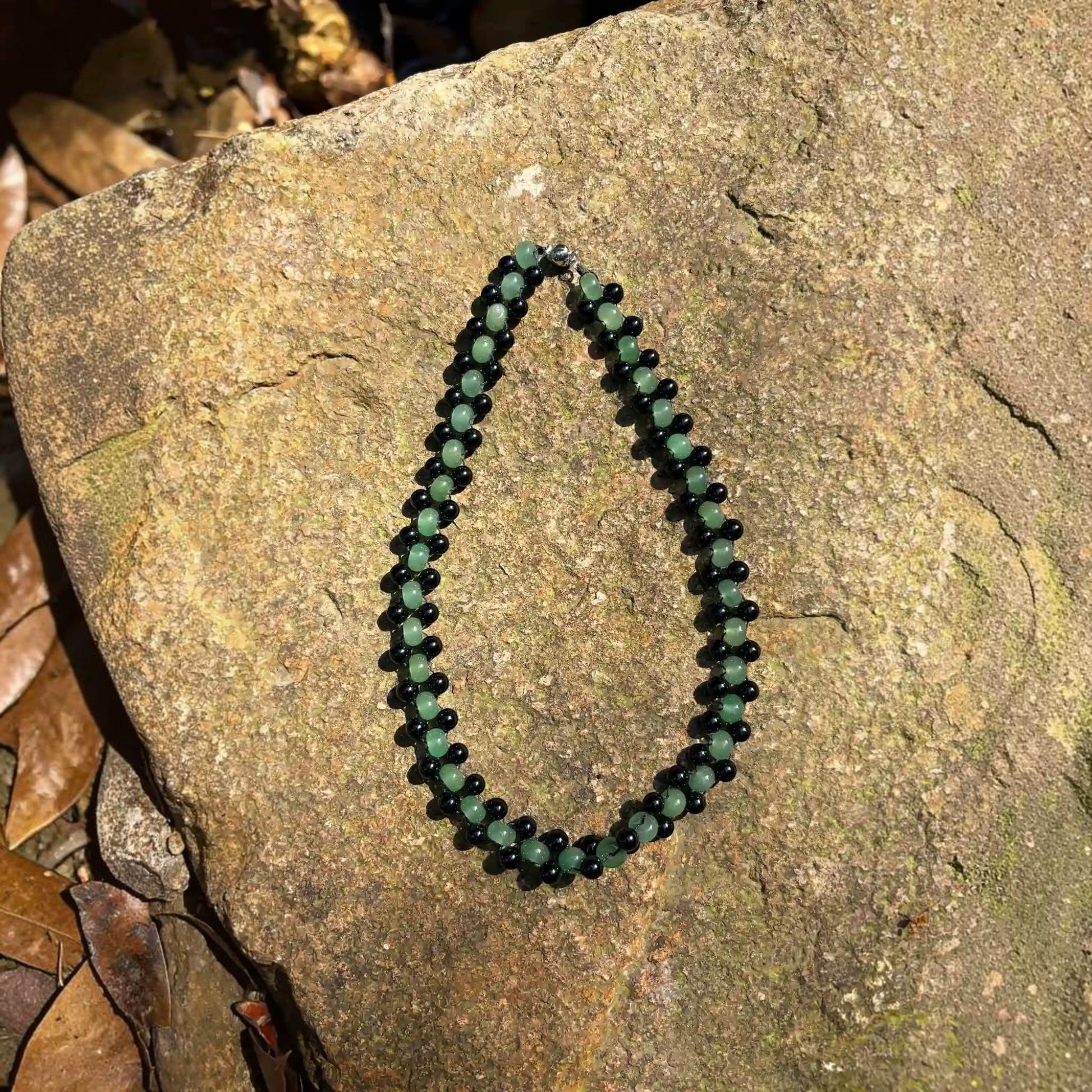 Hollywood Road Stories double strand choker featuring green jade and black lava stone beads on a textured rock surface.