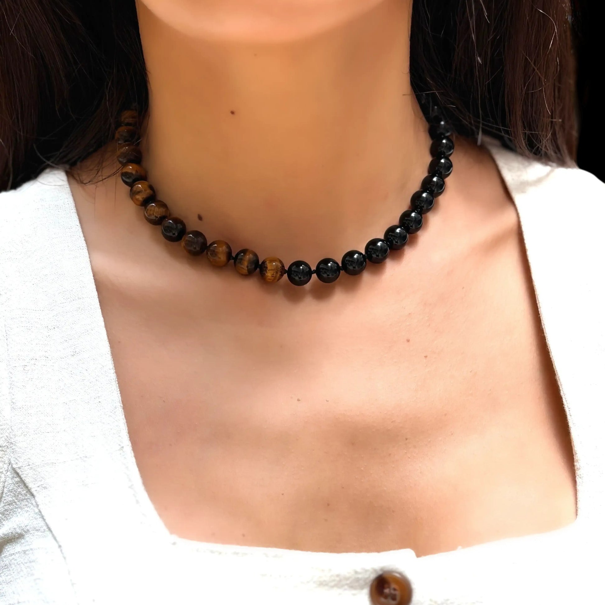 Statement necklace featuring polished black onyx and golden-brown tiger's eye stones on a model.