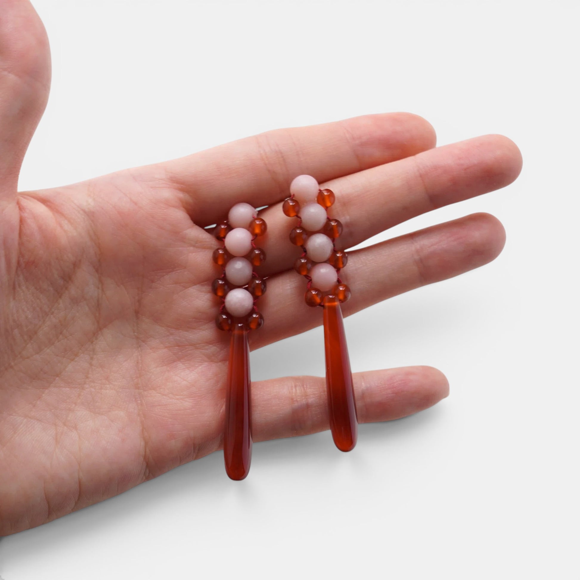 Hollywood Road Stories handcrafted drop earrings featuring pink beads and deep red teardrop accents held in a hand