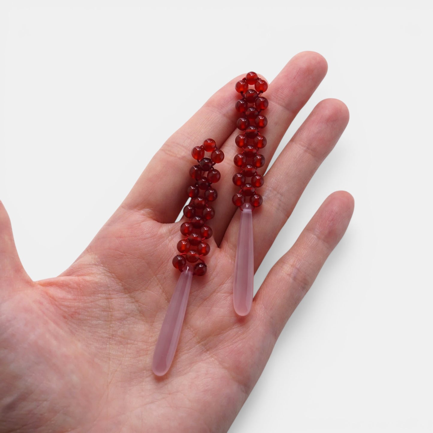 Hollywood Road Stories drop earrings with red beaded tops and smooth pale pink teardrop pendants held in a hand.