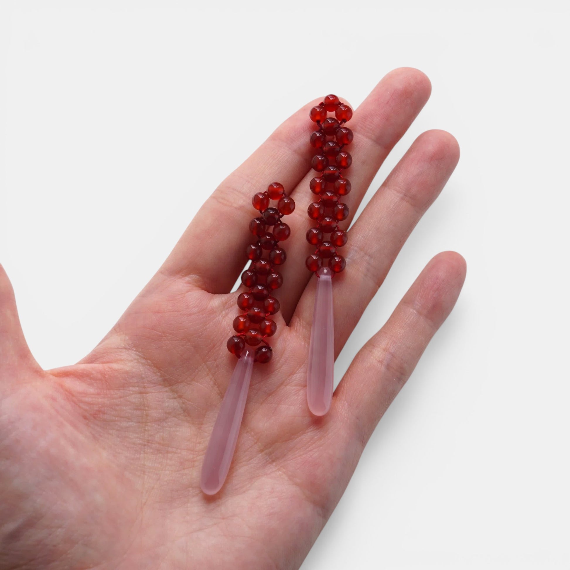 Hollywood Road Stories drop earrings with red beaded tops and smooth pale pink teardrop pendants held in a hand.
